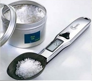 Digital measuring spoon with salt and a container of salt on a white background
