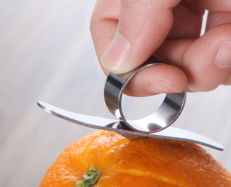 Hand using a metal orange peeler on an orange with a blurred background