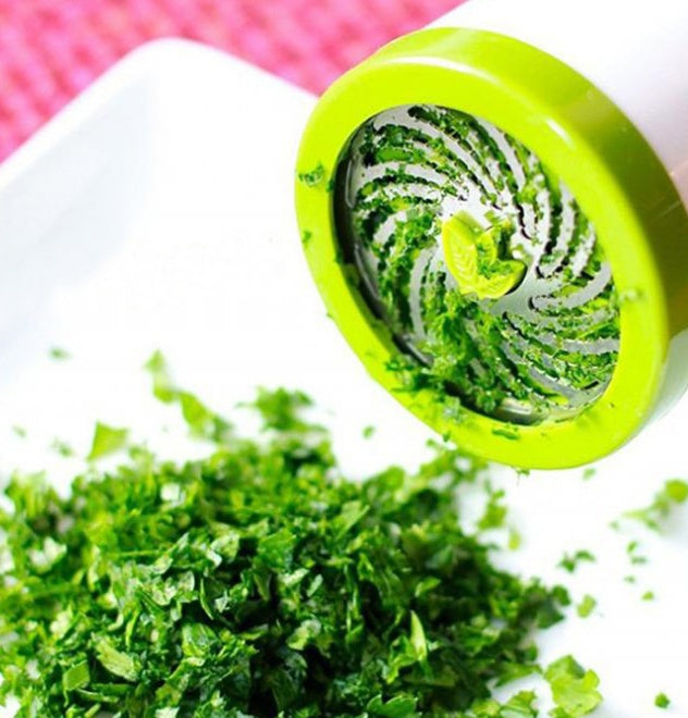 Green manual vegetable chopper with chopped greens on a white surface