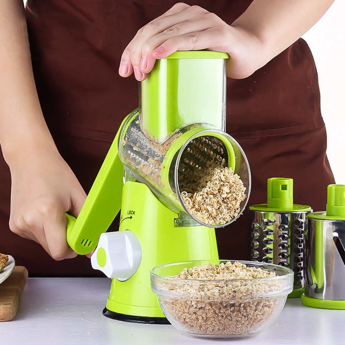 Person using a green manual grain grinder with a bowl of ground grains on a white surface.