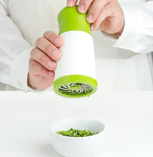 Person using a green and white manual herb grinder with a bowl of ground herbs on a white background