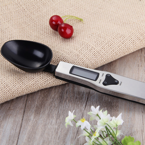 Digital measuring spoon on a wooden surface with a beige cloth and red berries in the background